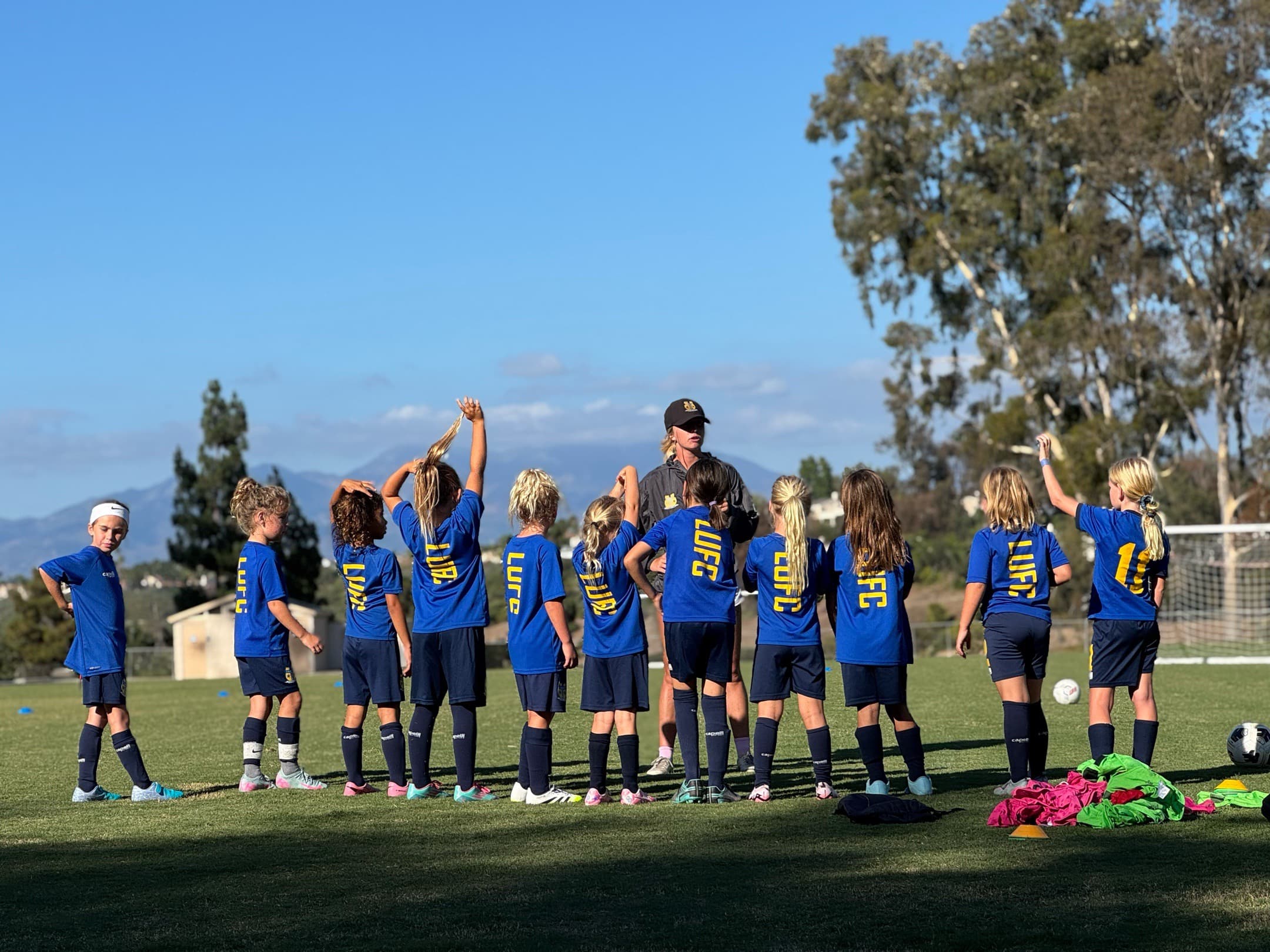 Coach Bella talking to a youth girls soccer team huddled on the field